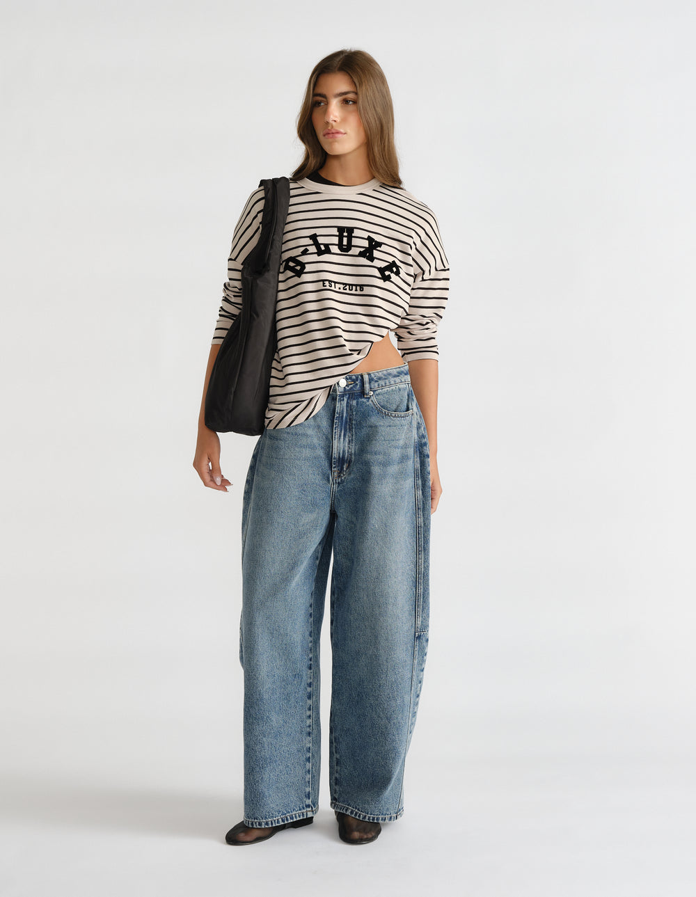 Woman wearing a striped long sleeve top with logo detail, paired with relaxed wide-leg blue jeans and a black shoulder bag