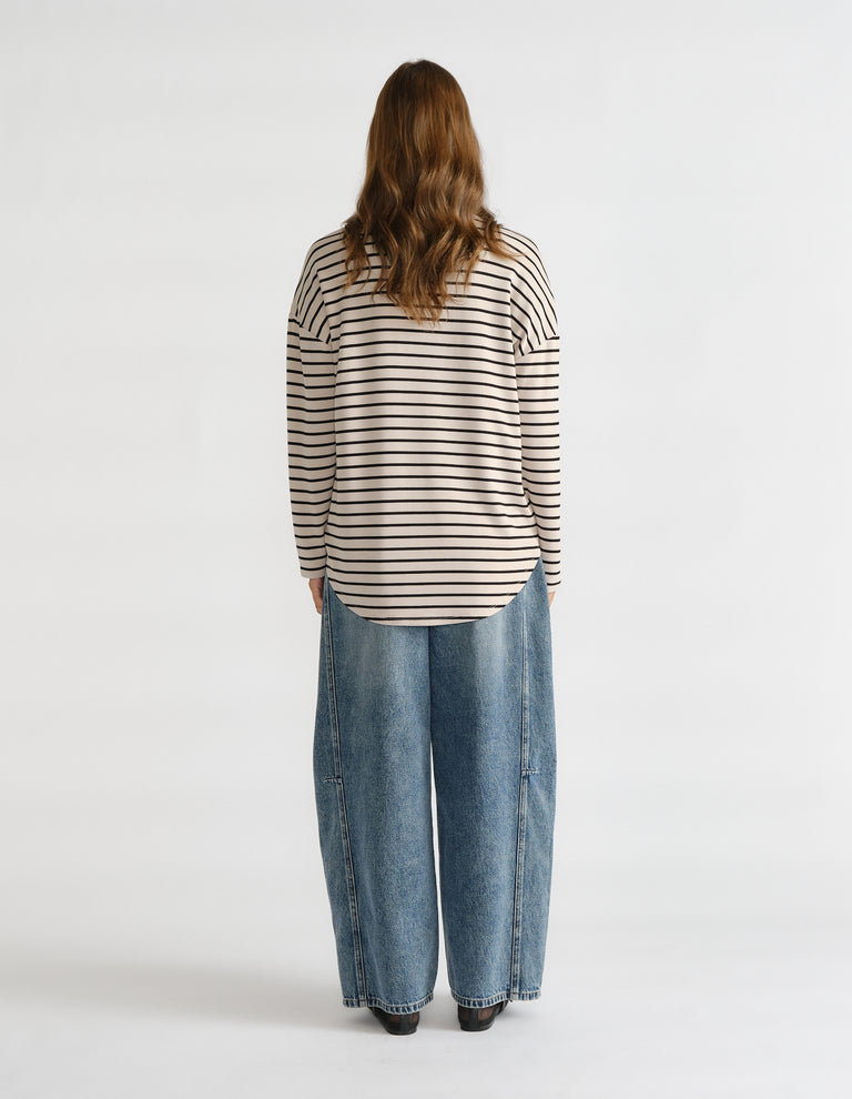 Back view of woman wearing a beige and black striped long sleeve top paired with wide-leg blue denim jeans and black shoes