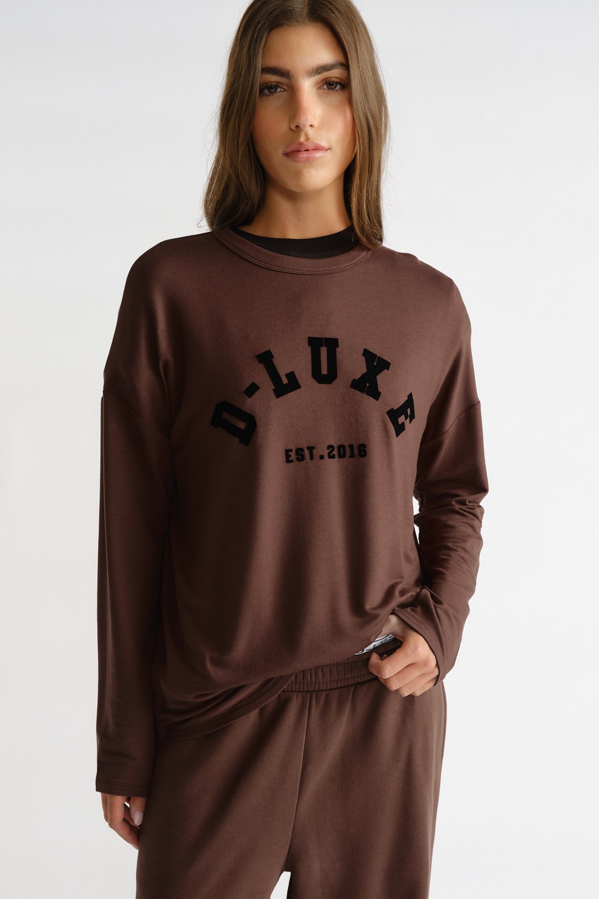 Woman wearing a relaxed-fit brown long sleeve top with bold D-Luxe lettering and matching casual pants