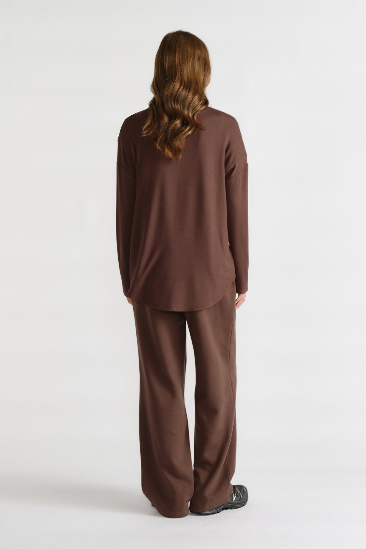 Woman seen from behind wearing relaxed long-sleeve brown top and matching wide-leg pants with black shoes