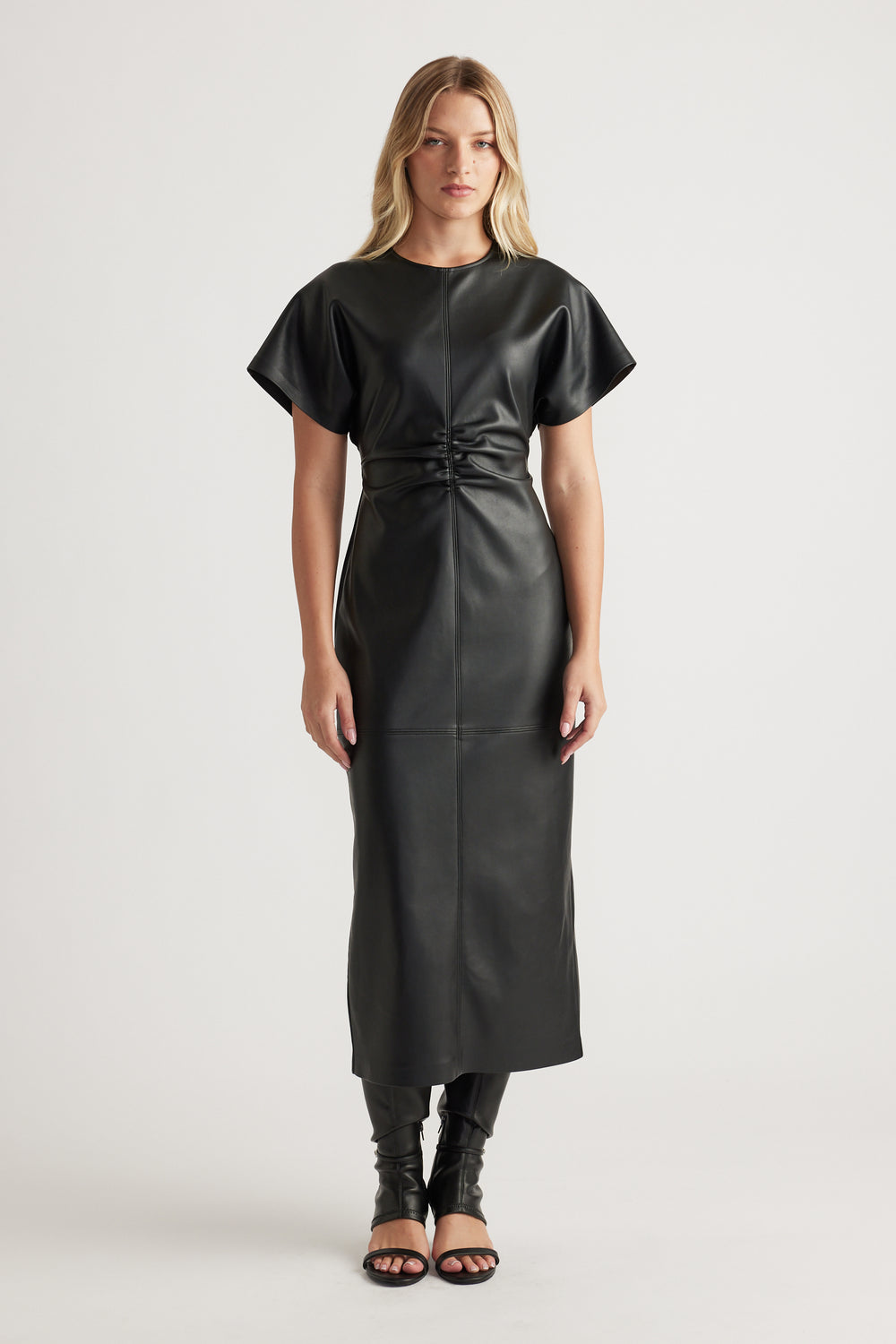 Woman wearing a sleek black faux leather midi dress with short sleeves and gathered waist detail styled with open-toe heels