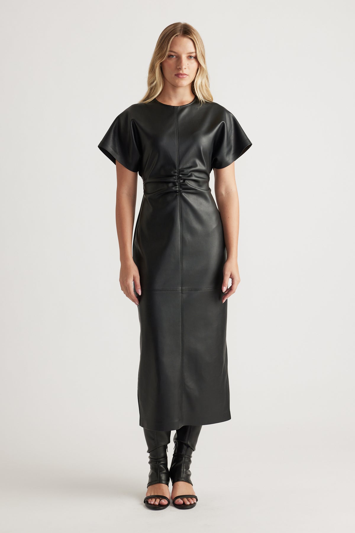 Woman wearing a sleek black faux leather midi dress with short sleeves and gathered waist detail styled with open-toe heels