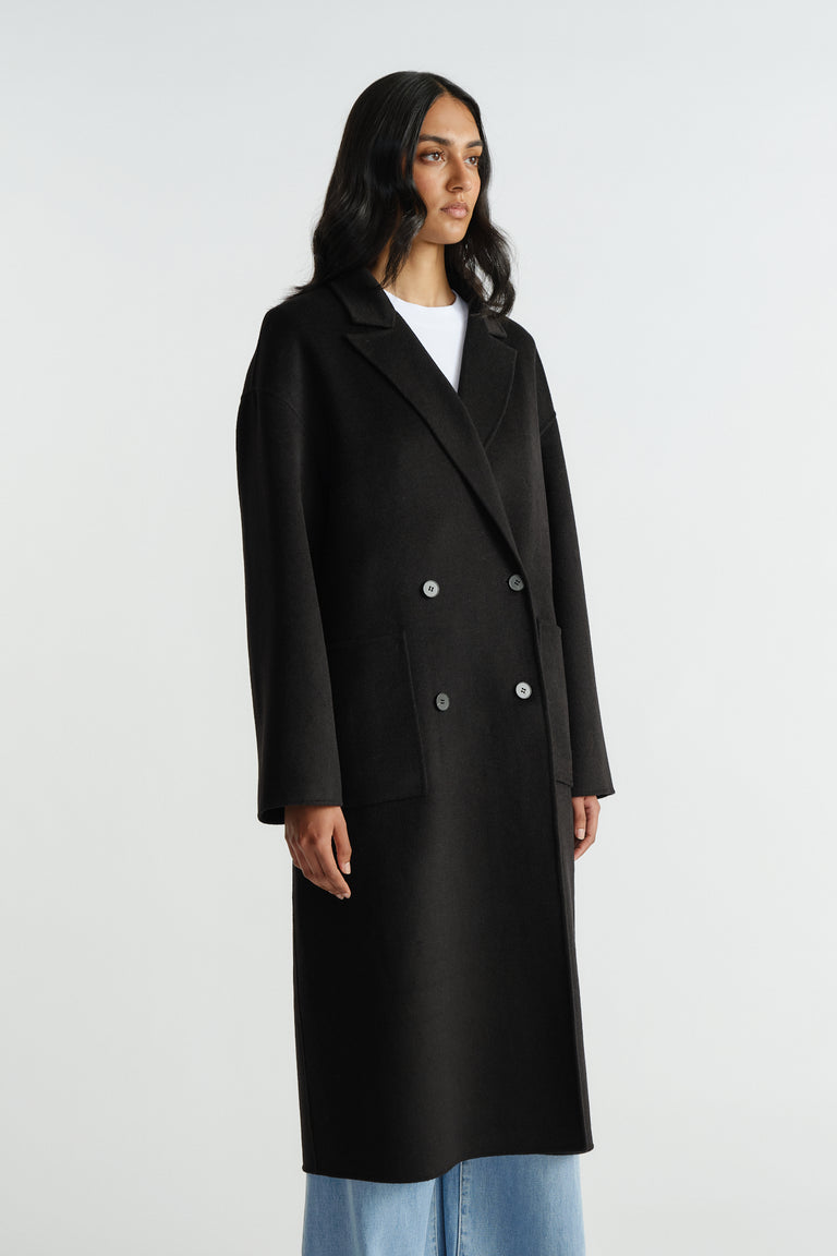 Woman wearing a long black double-breasted coat with structured lapels paired with light blue wide-leg jeans for a polished look