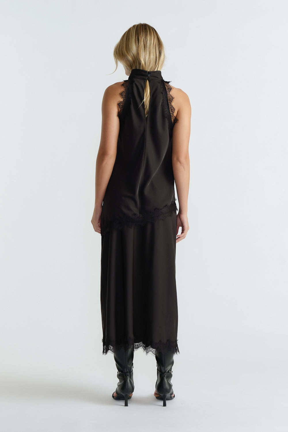 Woman seen from behind wearing a black halter top with lace edges paired with a matching midi skirt and black boots