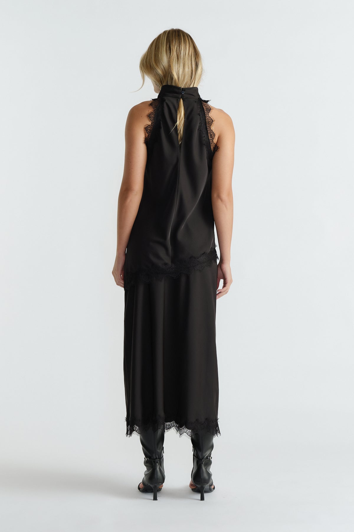 Woman seen from behind wearing a black halter top with lace edges paired with a matching midi skirt and black boots