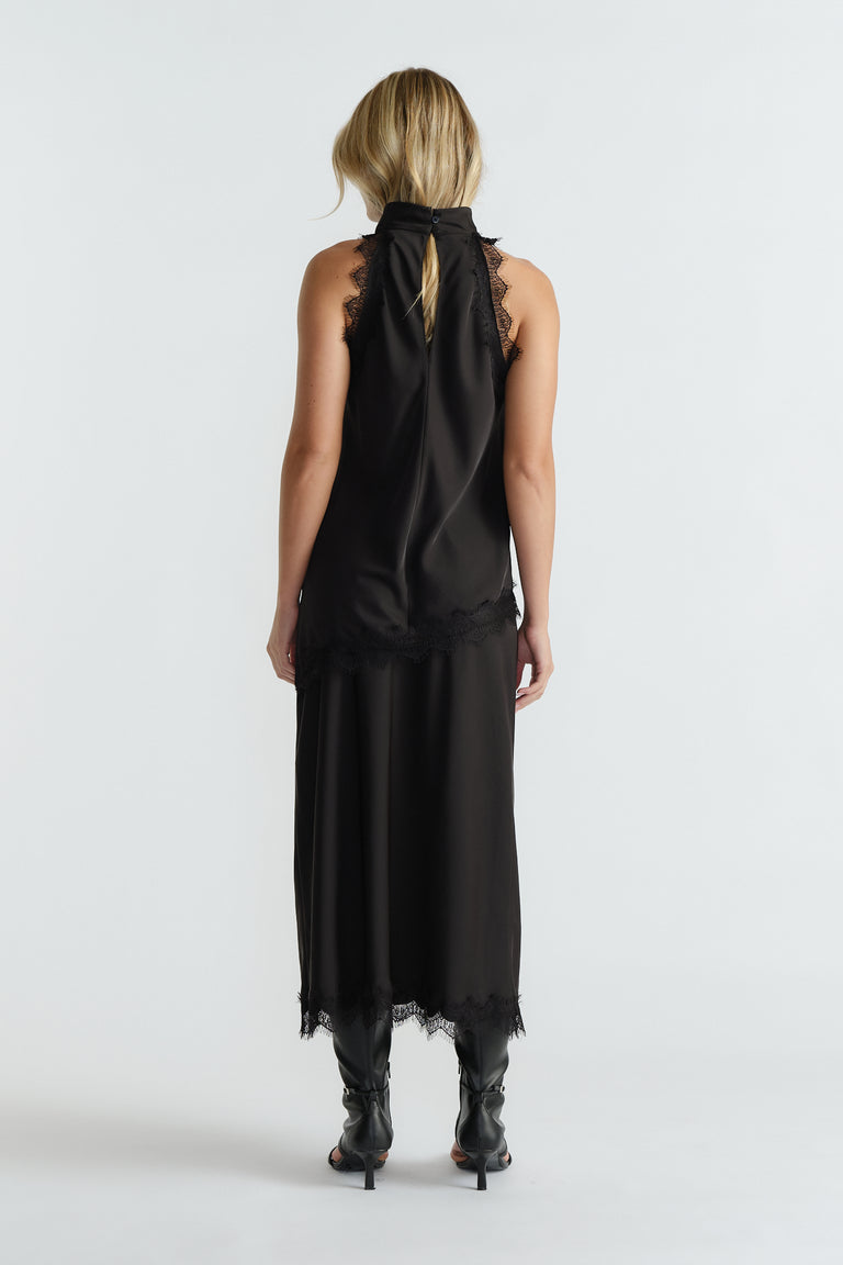 Woman seen from behind wearing a black halter top with lace edges paired with a matching midi skirt and black boots