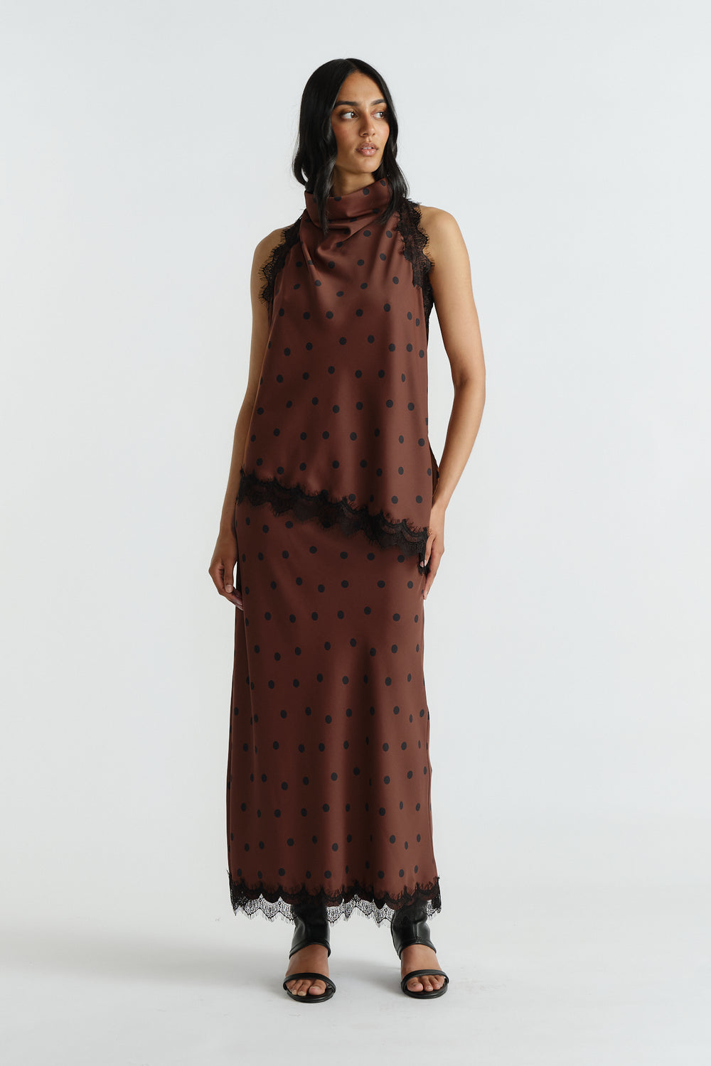 Woman wearing a brown polka dot halter top and matching skirt with black lace trim, styled with black open-toe sandals