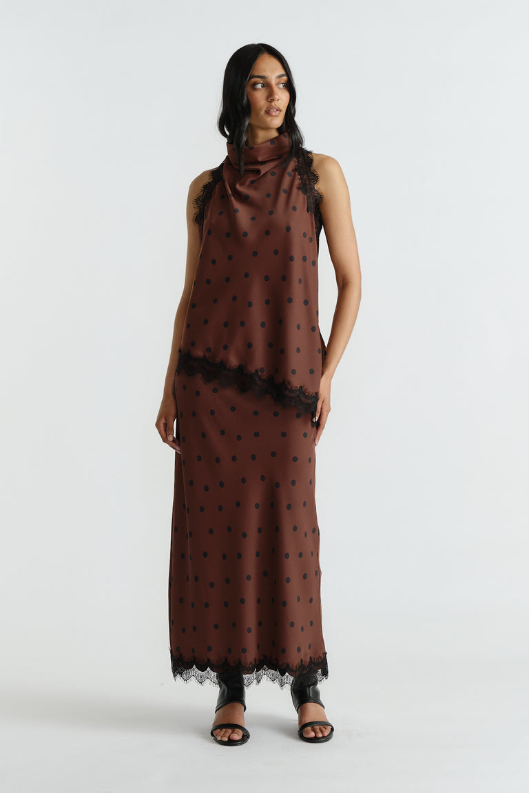 Woman wearing a brown polka dot halter top and matching skirt with black lace trim, styled with black open-toe sandals
