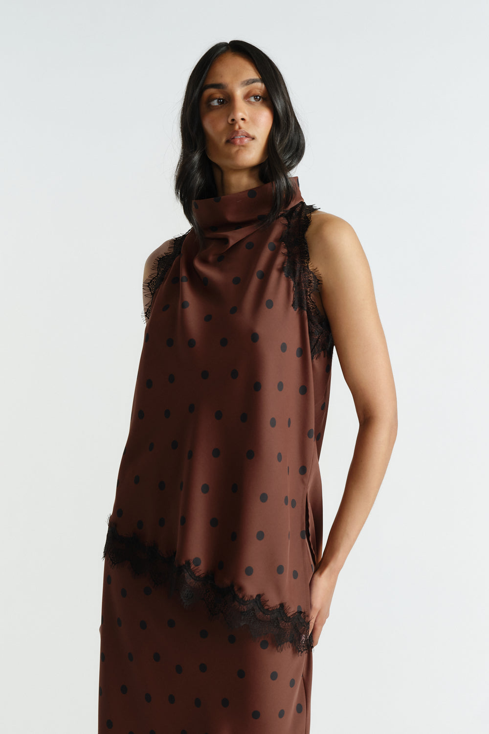 Woman wearing a brown halter top with black polka dots and delicate lace trim, styled for an elegant, effortless look