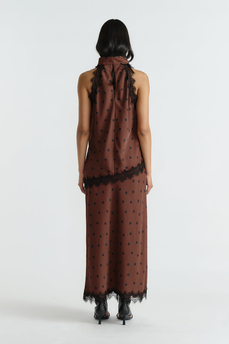 Back view of woman wearing a sleeveless brown polka dot halter top and matching skirt with black lace trim and heels