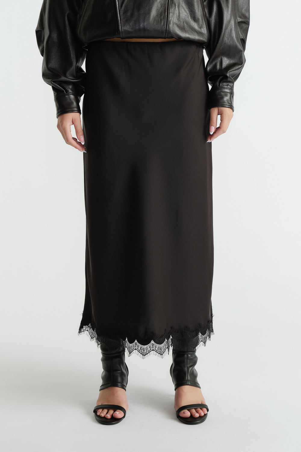 Black midi skirt featuring delicate lace trim at hem, styled with a cropped leather jacket and open-toe heels.