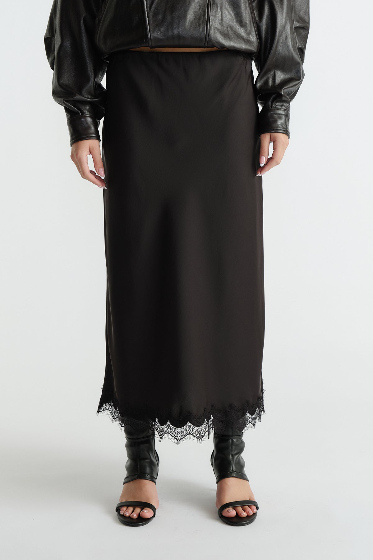 Black midi skirt featuring delicate lace trim at hem, styled with a cropped leather jacket and open-toe heels.