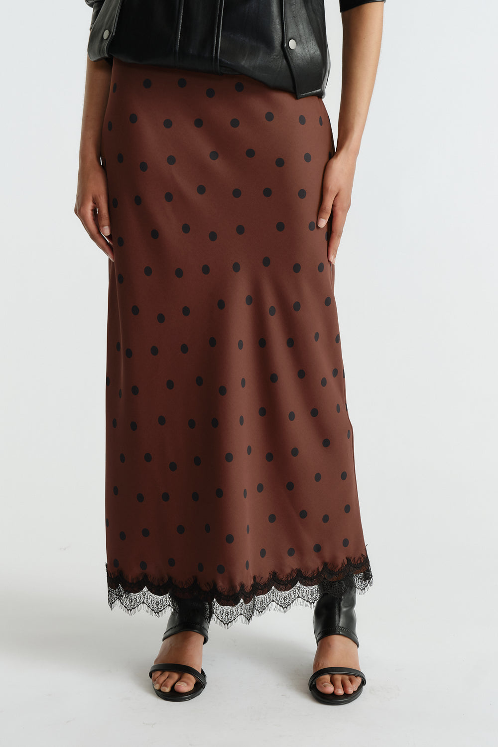 Brown maxi skirt with black polka dots and delicate lace trim, styled with a black leather jacket and open-toe sandals