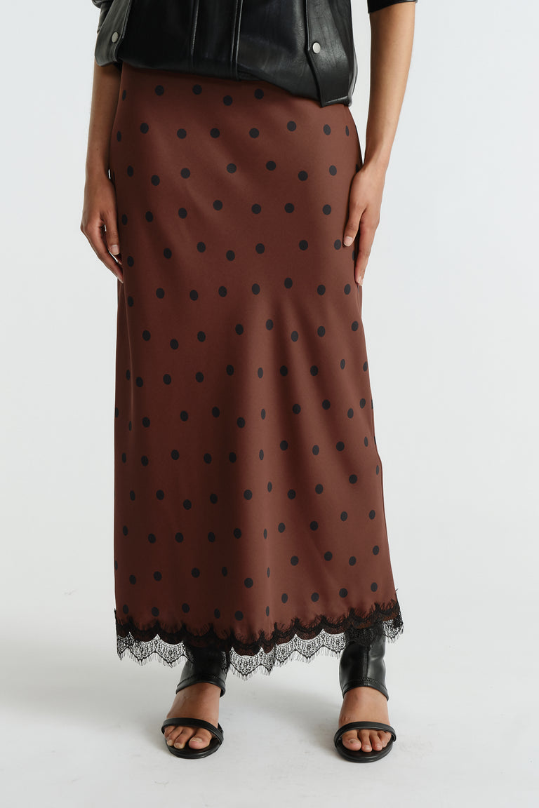 Brown maxi skirt with black polka dots and delicate lace trim, styled with a black leather jacket and open-toe sandals