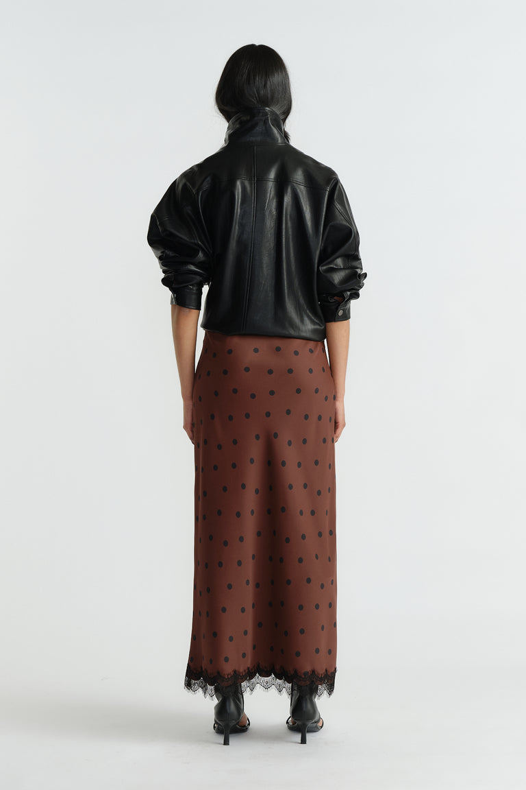 Back view of woman wearing a brown maxi skirt with black polka dots and lace trim paired with a black leather jacket