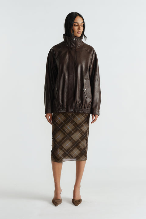 Woman wearing a knee-length caramel check mesh skirt paired with a loose dark brown leather jacket and pointed heels