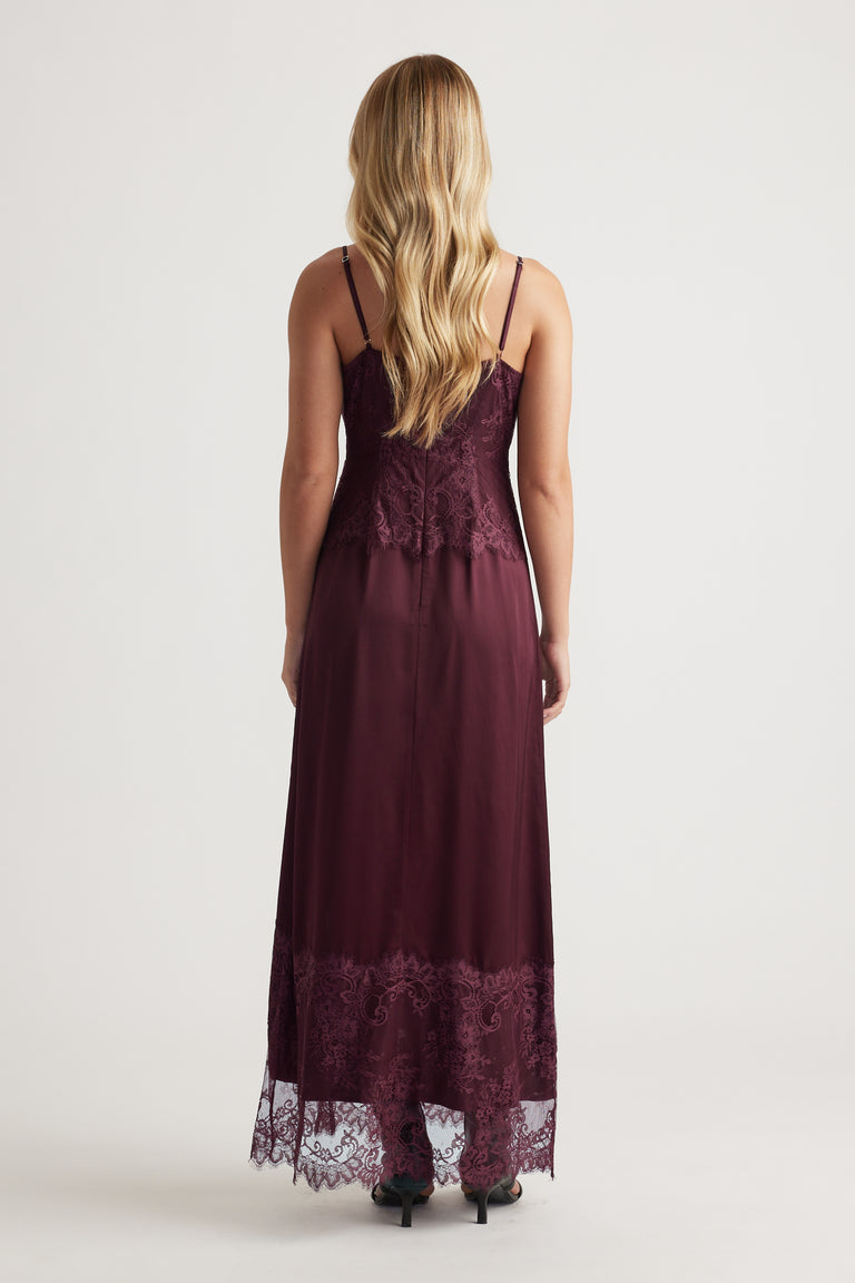 Back view of a sleeveless plum maxi dress with delicate lace detailing and thin adjustable straps, styled with heels.