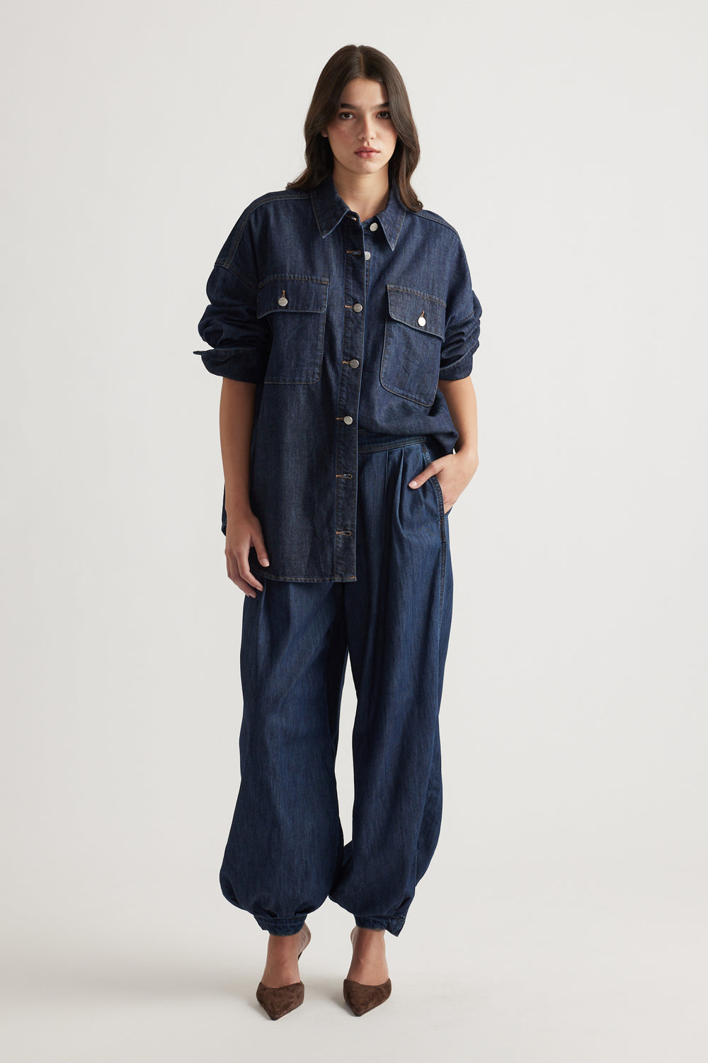Woman wearing oversized dark denim shirt with large pockets and relaxed cuffed denim pants styled with brown heels