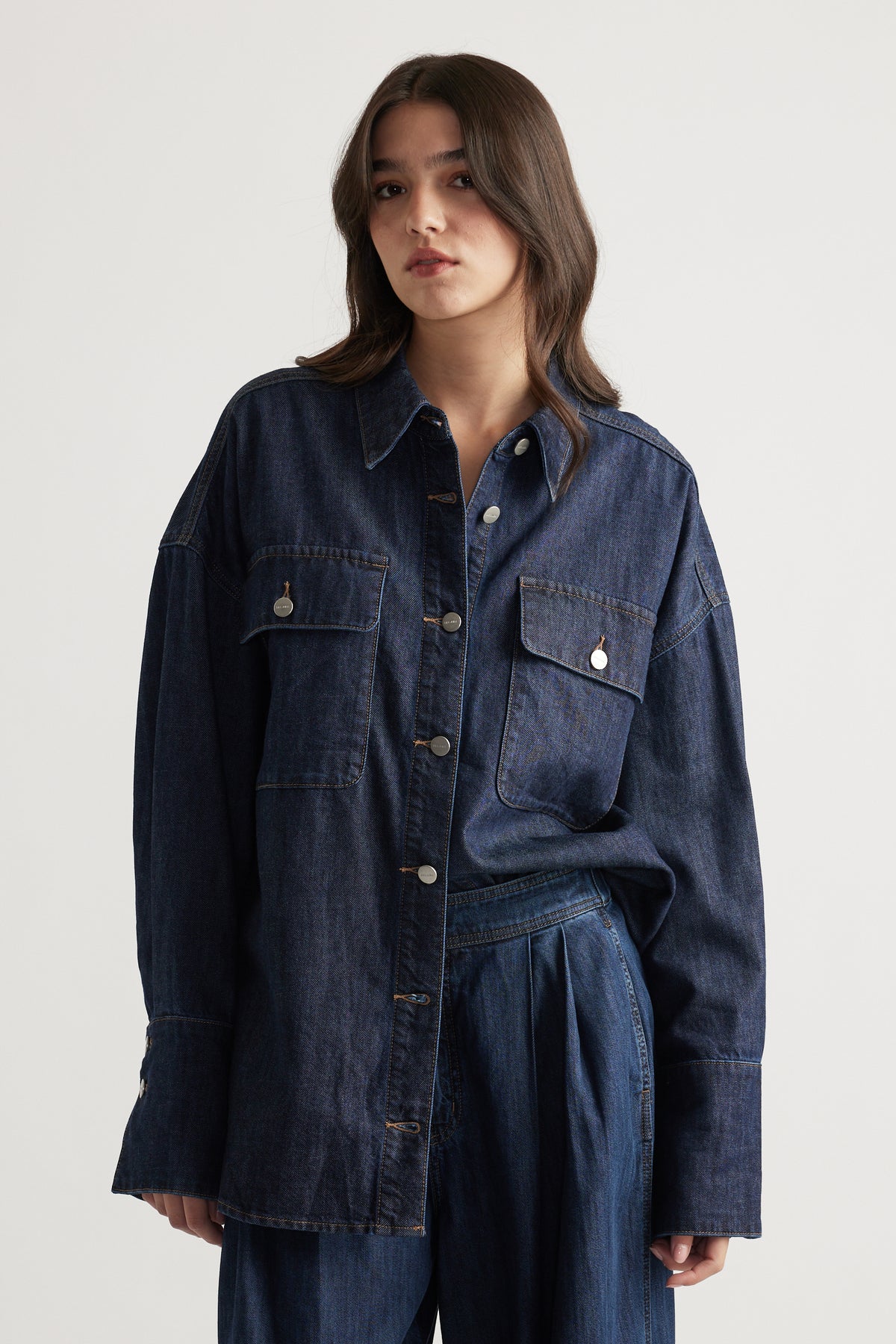 Woman wearing a relaxed dark denim shirt with large flap pockets and silver buttons, styled with matching wide-leg pants
