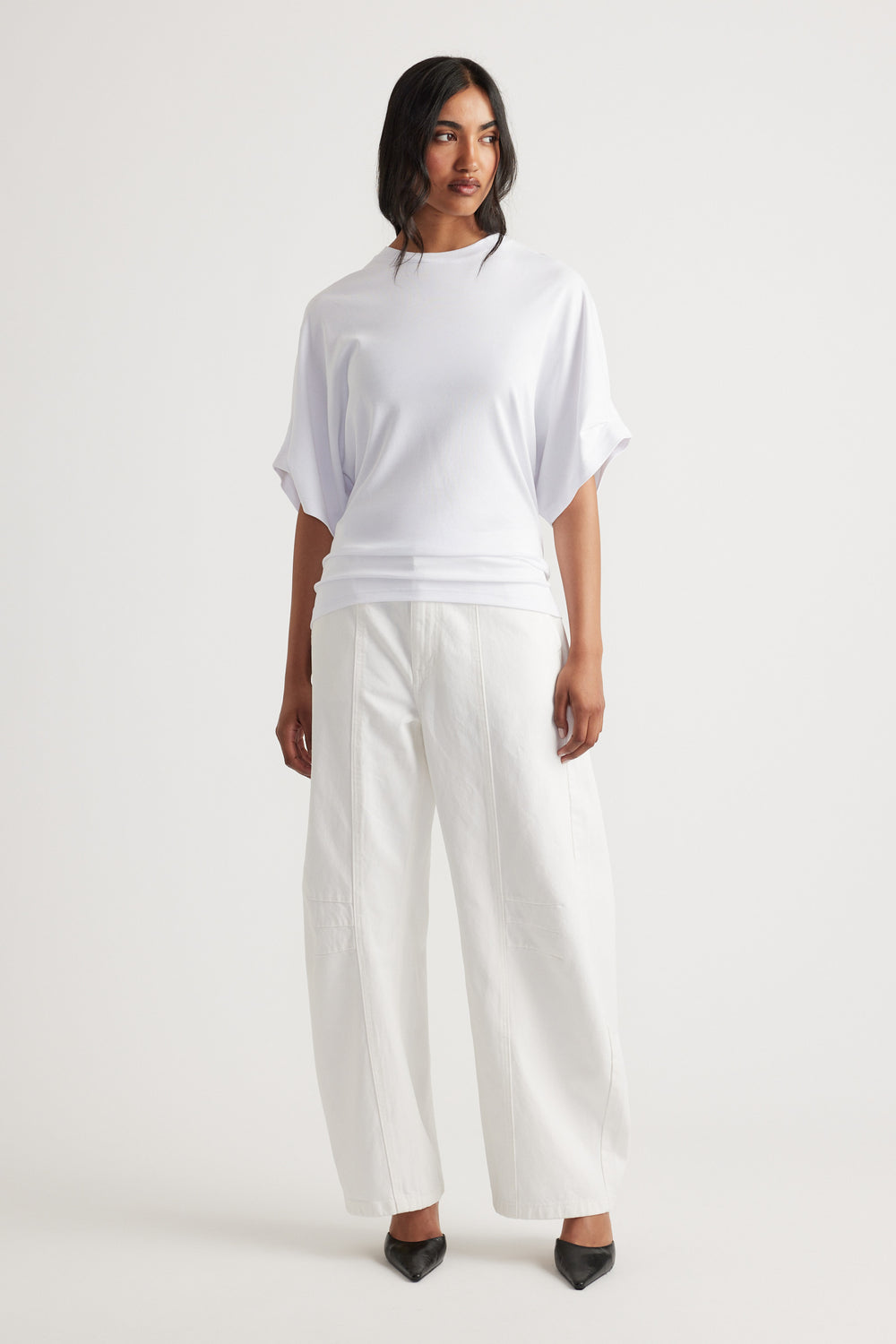 Woman wearing a relaxed white tee with rolled short sleeves paired with wide-leg white pants and black pointed shoes