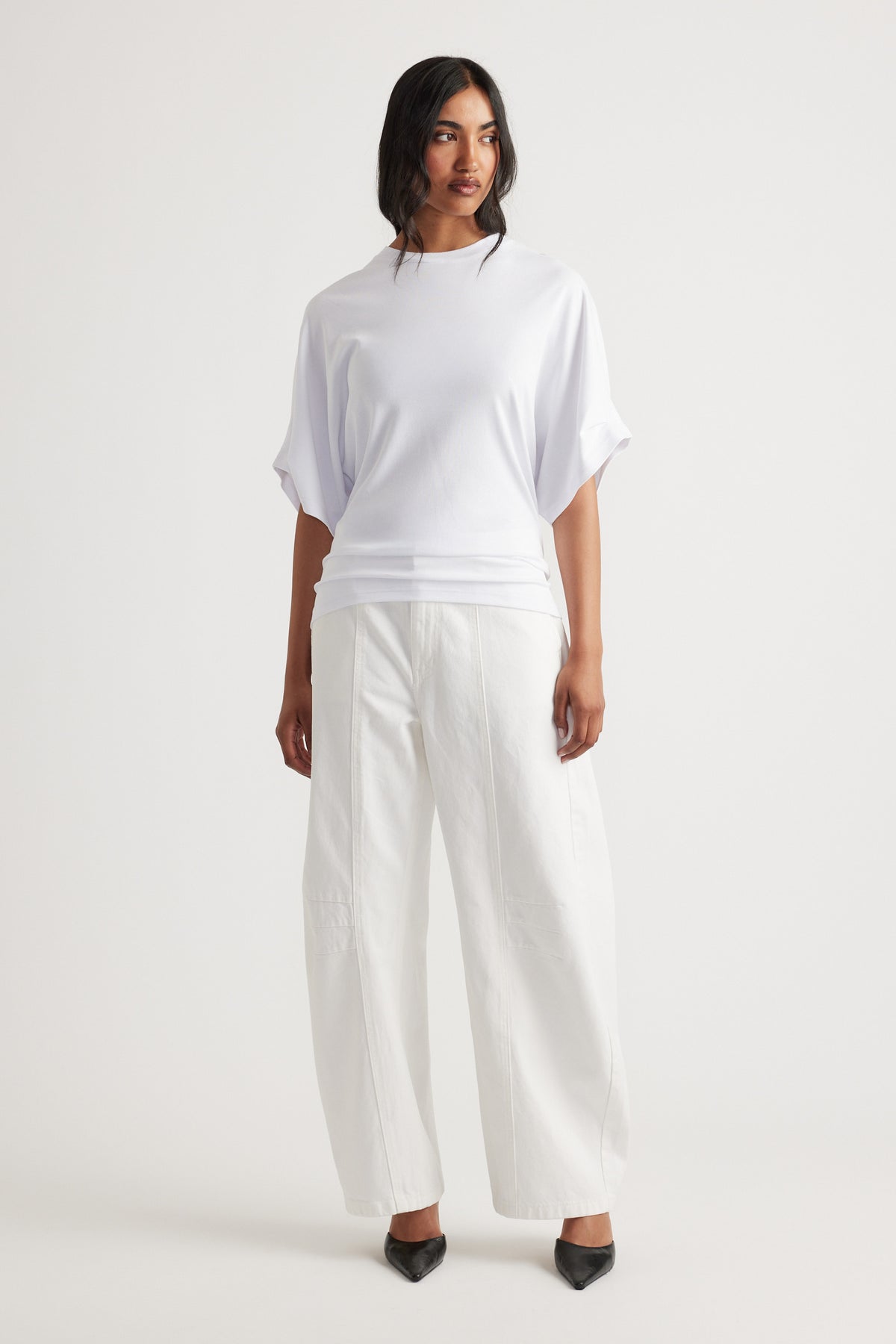 Woman wearing a relaxed white tee with rolled short sleeves paired with wide-leg white pants and black pointed shoes