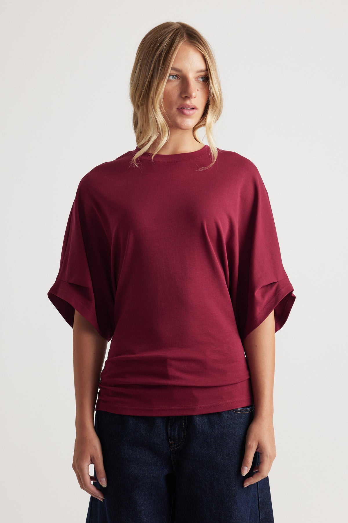 Relaxed fit deep red tee with wide short sleeves and a simple crew neckline paired with dark denim jeans
