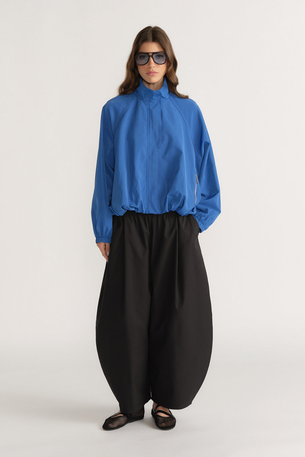 Woman wearing a loose fit blue zipped jacket with high neck paired with voluminous black wide-leg pants and flats