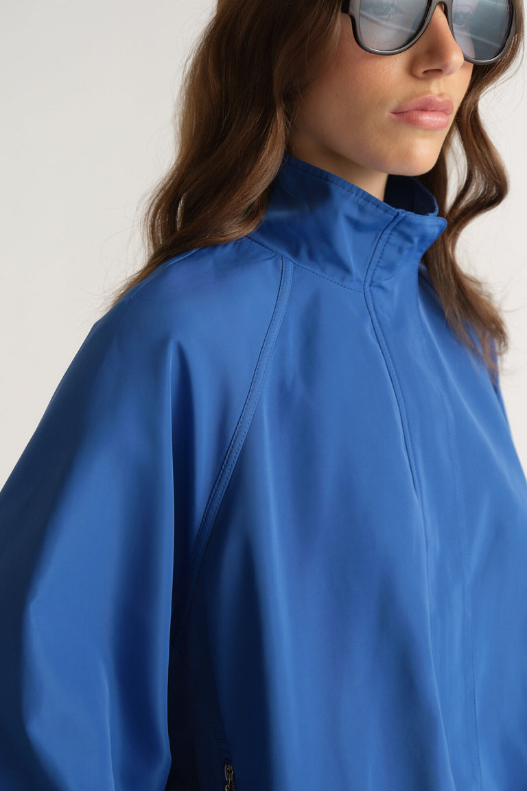 Close-up of woman wearing a vibrant blue oversized jacket with high neck and raglan seam detail and sunglasses