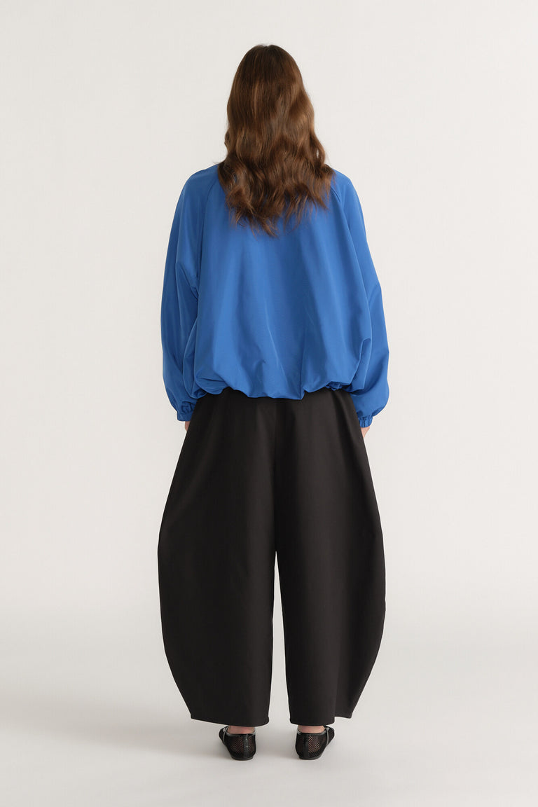 Woman seen from back wearing a loose blue long-sleeve top and wide-leg black pants with flat shoes