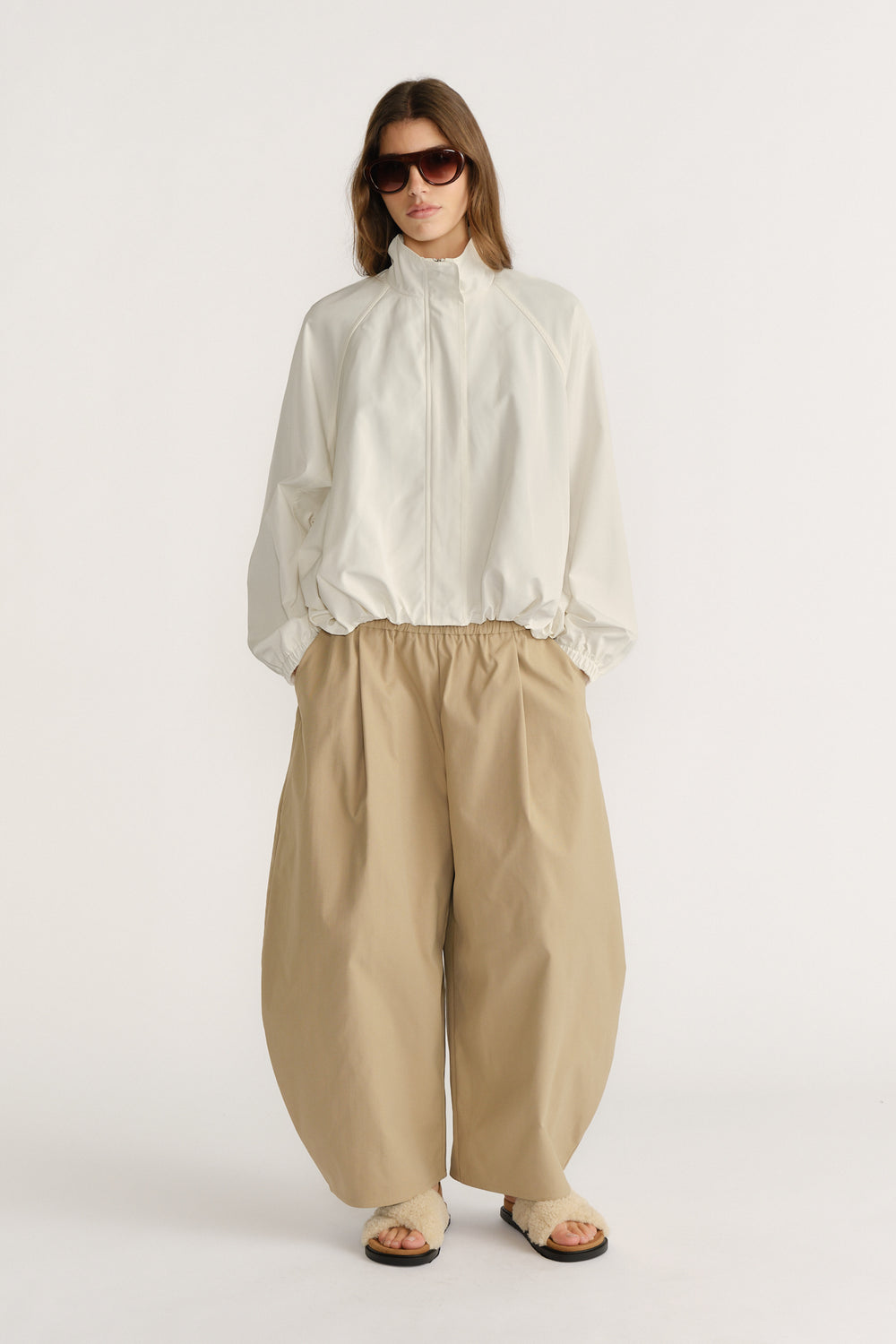 Woman wearing a relaxed ivory spray jacket with elastic cuffs paired with wide-leg beige pants and sandals