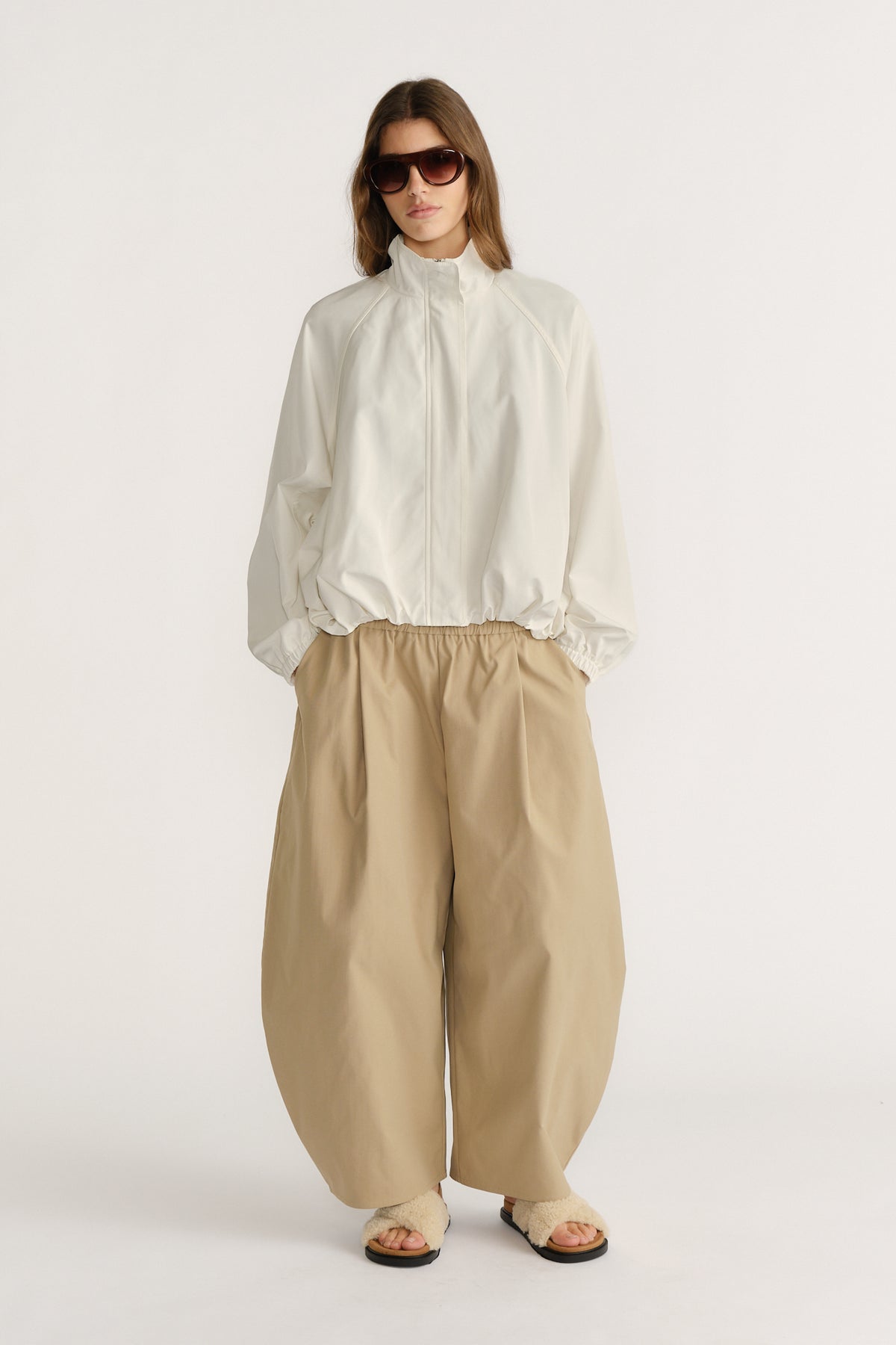 Woman wearing a relaxed ivory spray jacket with elastic cuffs paired with wide-leg beige pants and sandals