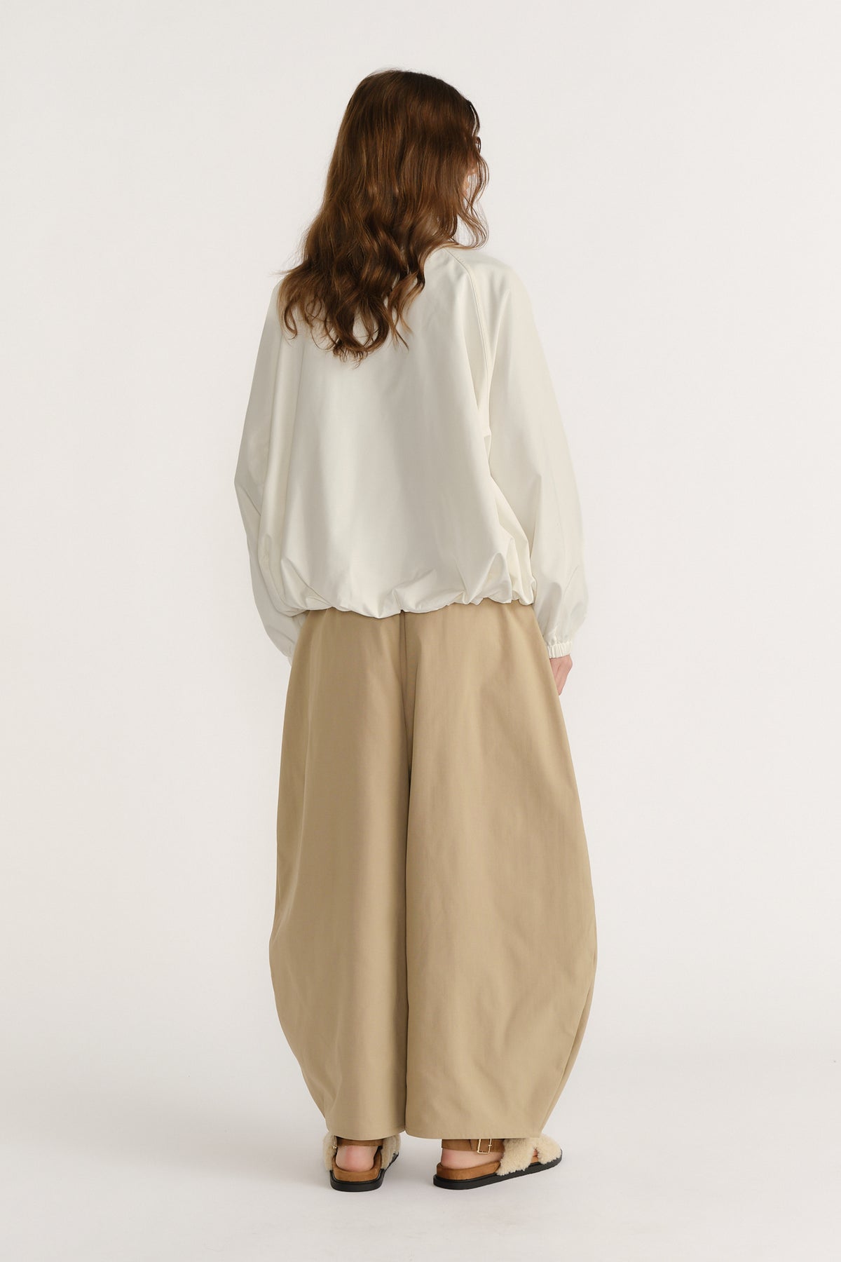 Woman wearing a relaxed ivory spray jacket with elastic hem paired with wide-leg beige trousers and casual sandals