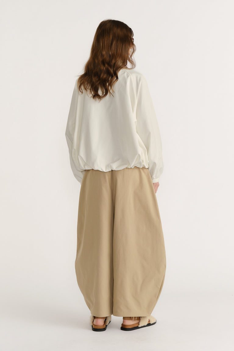 Woman wearing a relaxed ivory spray jacket with elastic hem paired with wide-leg beige trousers and casual sandals