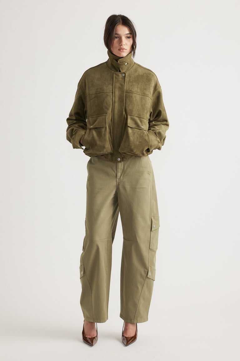 Woman wearing an olive faux suede bomber jacket with a high collar paired with relaxed-fit khaki cargo pants and brown heels