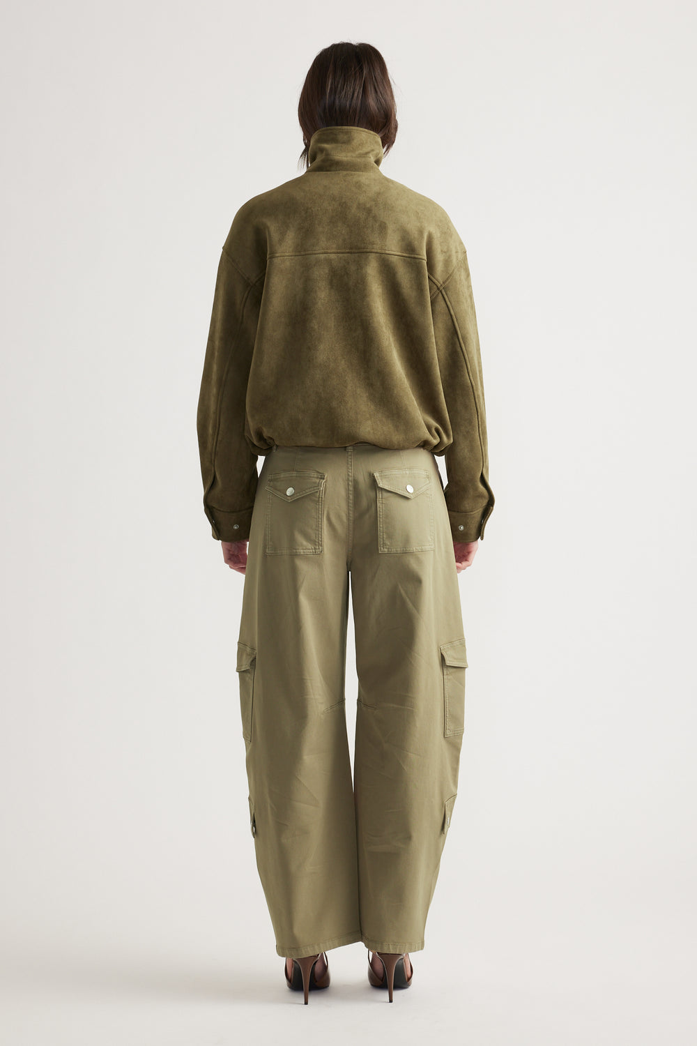 Back view of a woman wearing an olive faux suede jacket with relaxed fit khaki cargo pants and heels