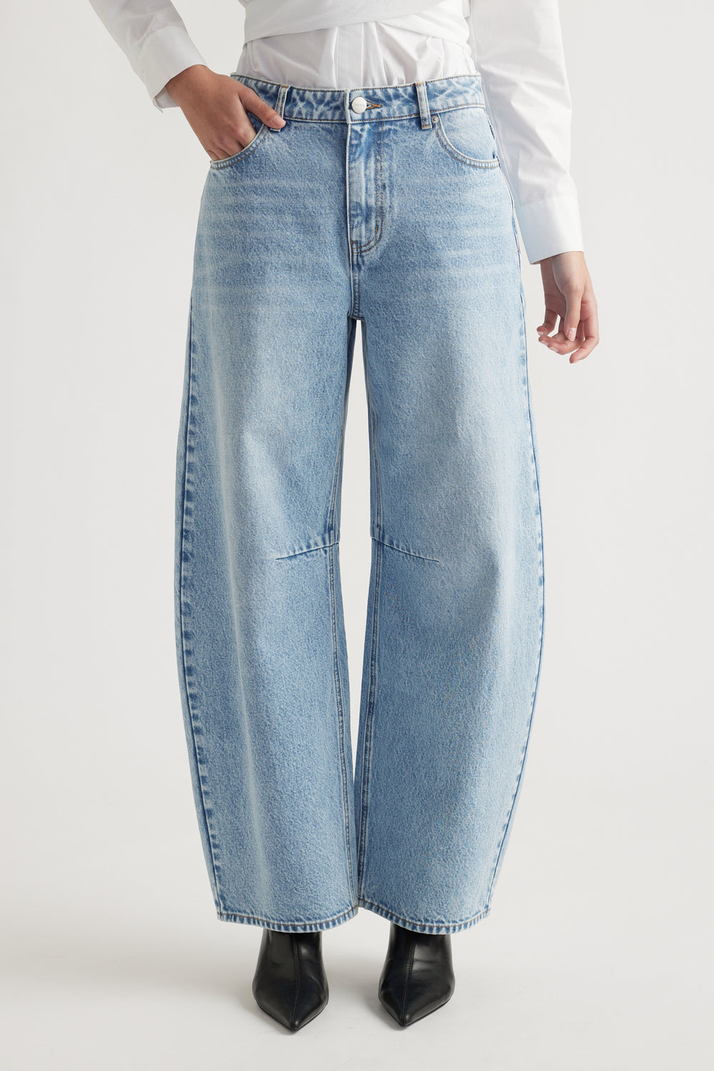 Woman wearing light blue wide-leg denim jeans paired with black pointed boots and a white shirt