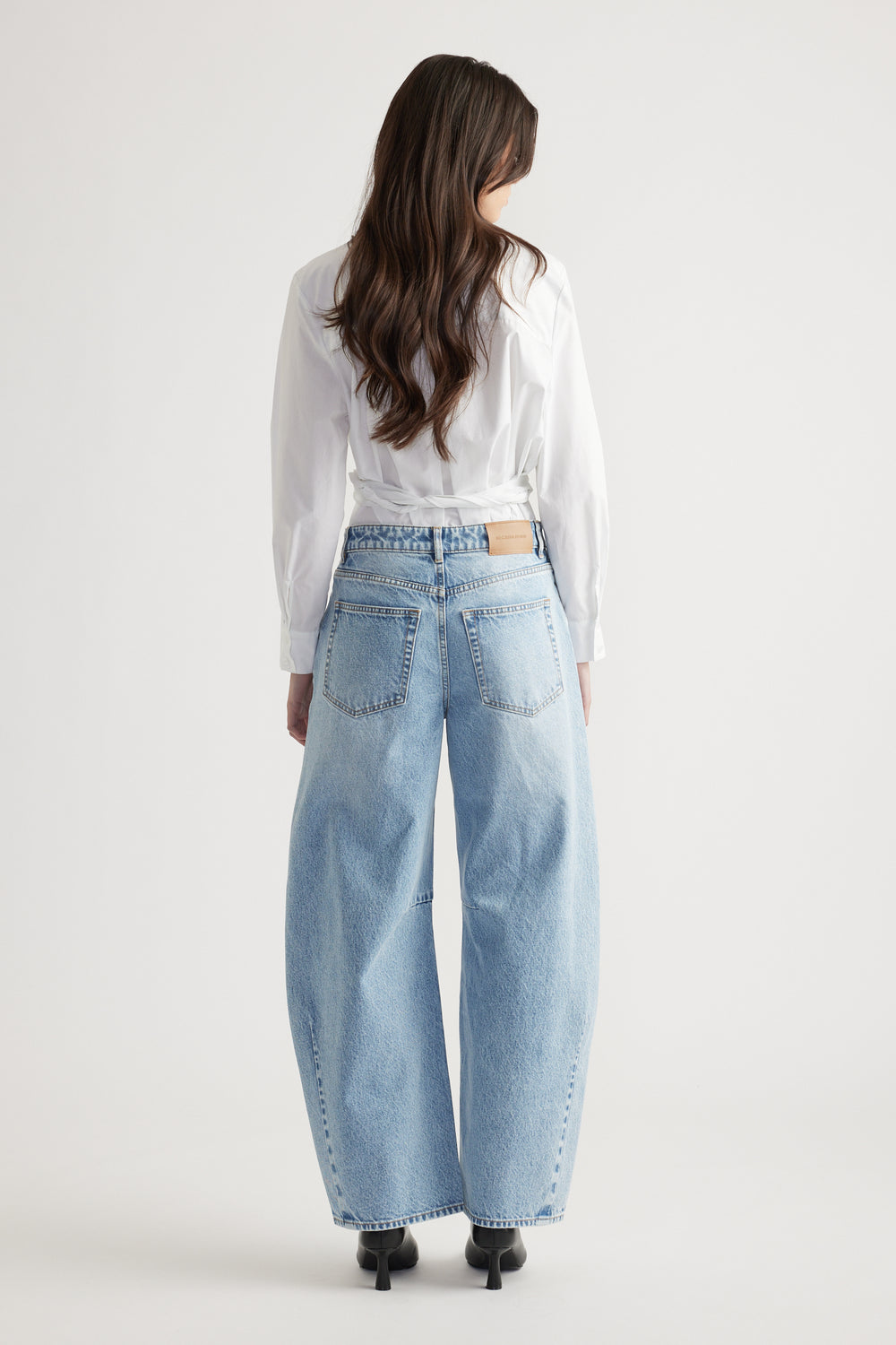 Woman wearing light wash wide-leg jeans paired with a crisp white long-sleeve blouse and black heeled boots.