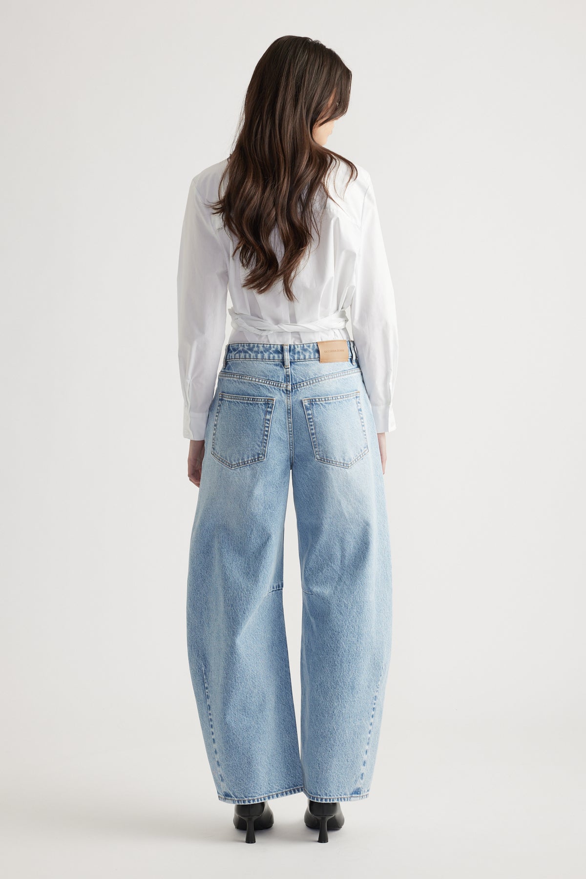 Woman wearing light wash wide-leg jeans paired with a crisp white long-sleeve blouse and black heeled boots.