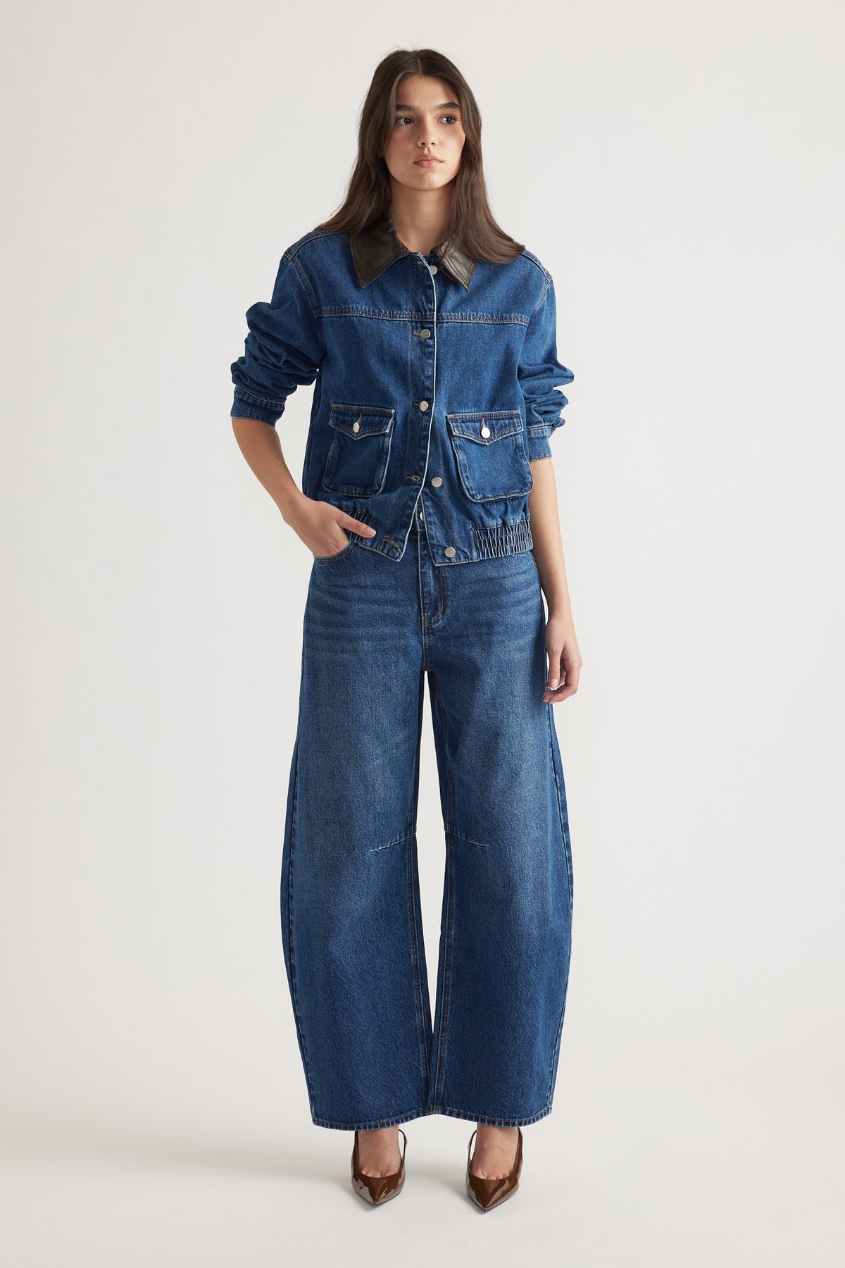 Woman wearing a dark indigo denim jacket with a brown collar and wide-leg jeans styled with pointed brown heels