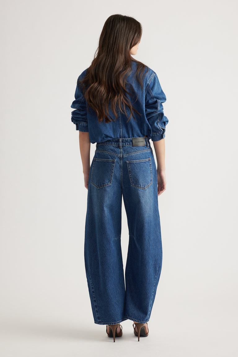 Woman seen from behind wearing wide-leg indigo denim jeans and a matching jacket with long sleeves rolled up.