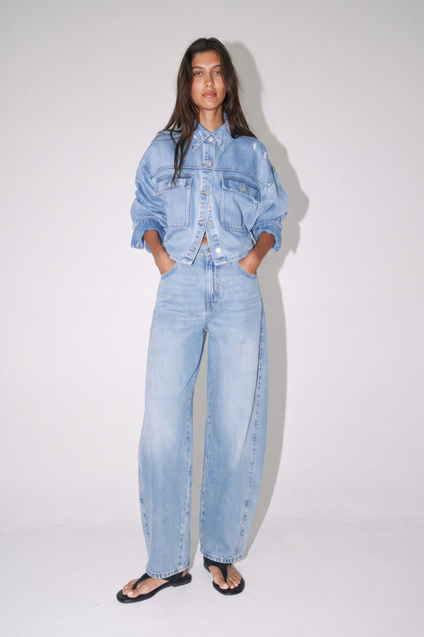 Woman wearing a light blue denim jacket with matching mid-rise barrel jeans and black sandals