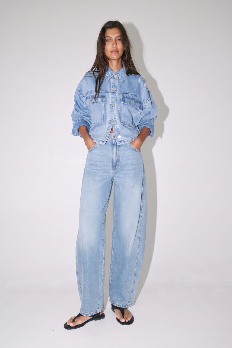 Woman wearing a light blue denim jacket with matching mid-rise barrel jeans and black sandals
