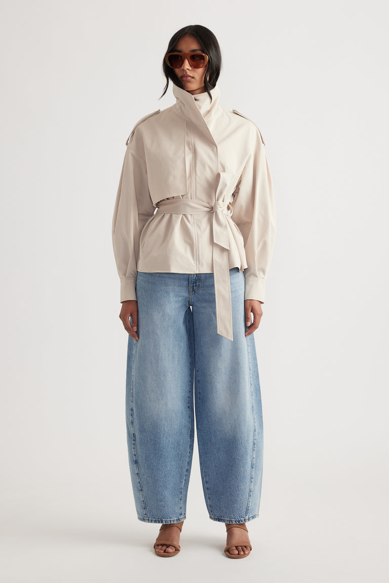Front view of woman wearing light blue wide-leg mid rise jeans paired with beige belted jacket and brown sandals