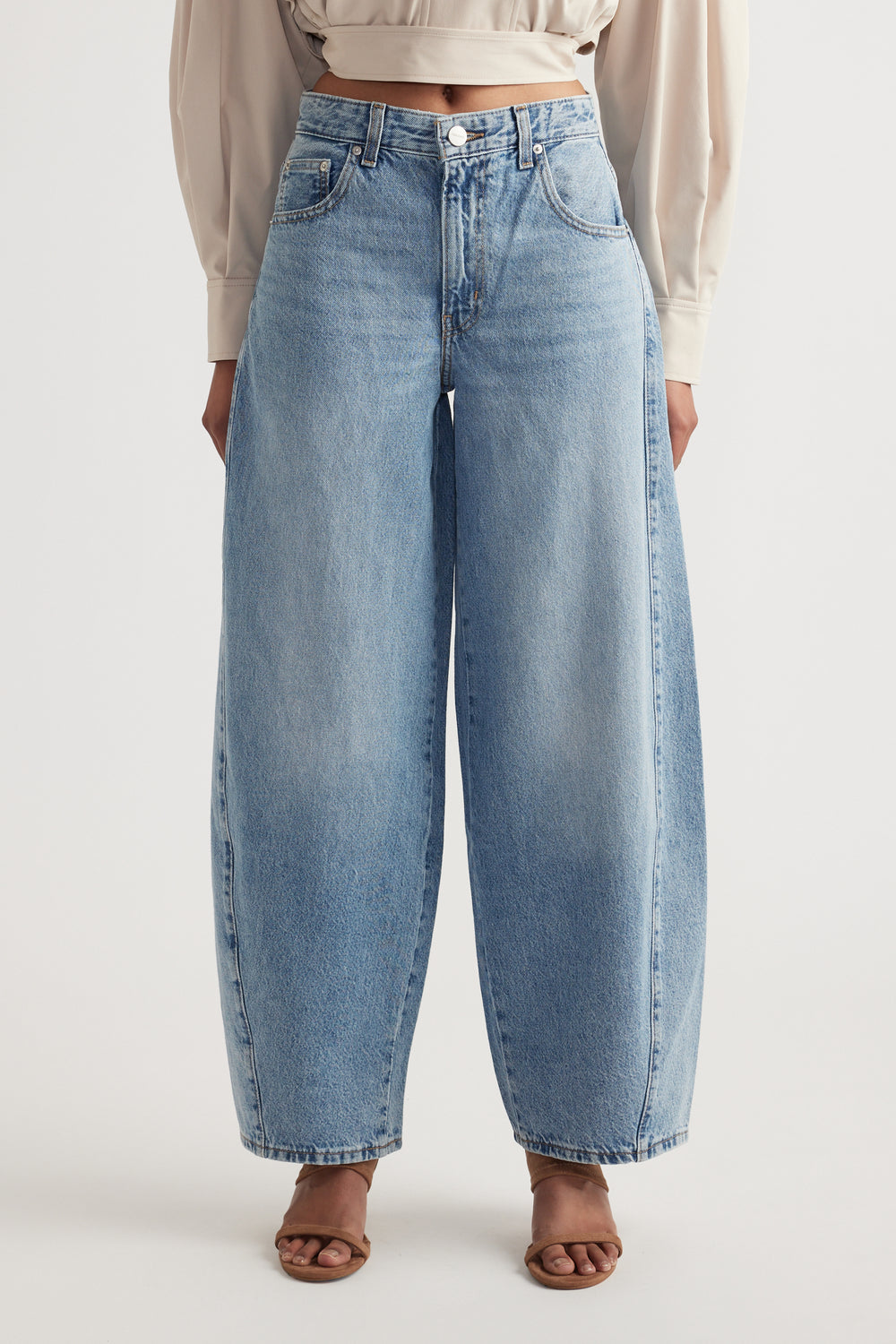Front view of woman wearing mid rise wide leg light blue denim jeans with sculptural seam details and tan sandals