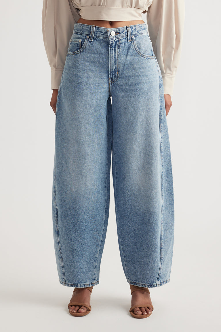 Front view of woman wearing mid rise wide leg light blue denim jeans with sculptural seam details and tan sandals