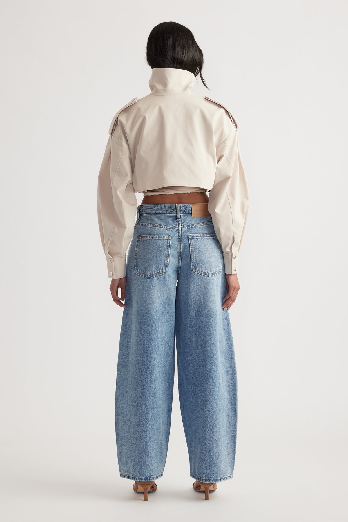 Rear view of woman wearing mid rise wide-leg light wash denim jeans with a cropped beige jacket and heels