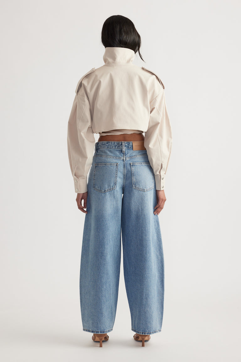 Rear view of woman wearing mid rise wide-leg light wash denim jeans with a cropped beige jacket and heels