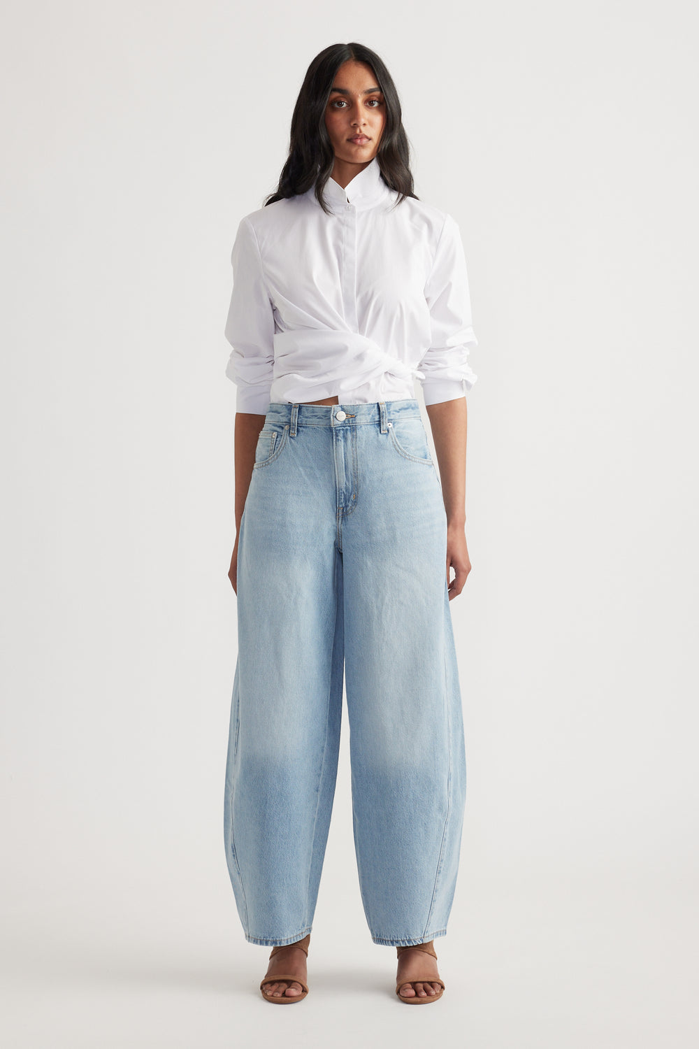 Woman wearing light wash wide-leg denim jeans with a white button-up shirt tucked and rolled sleeves