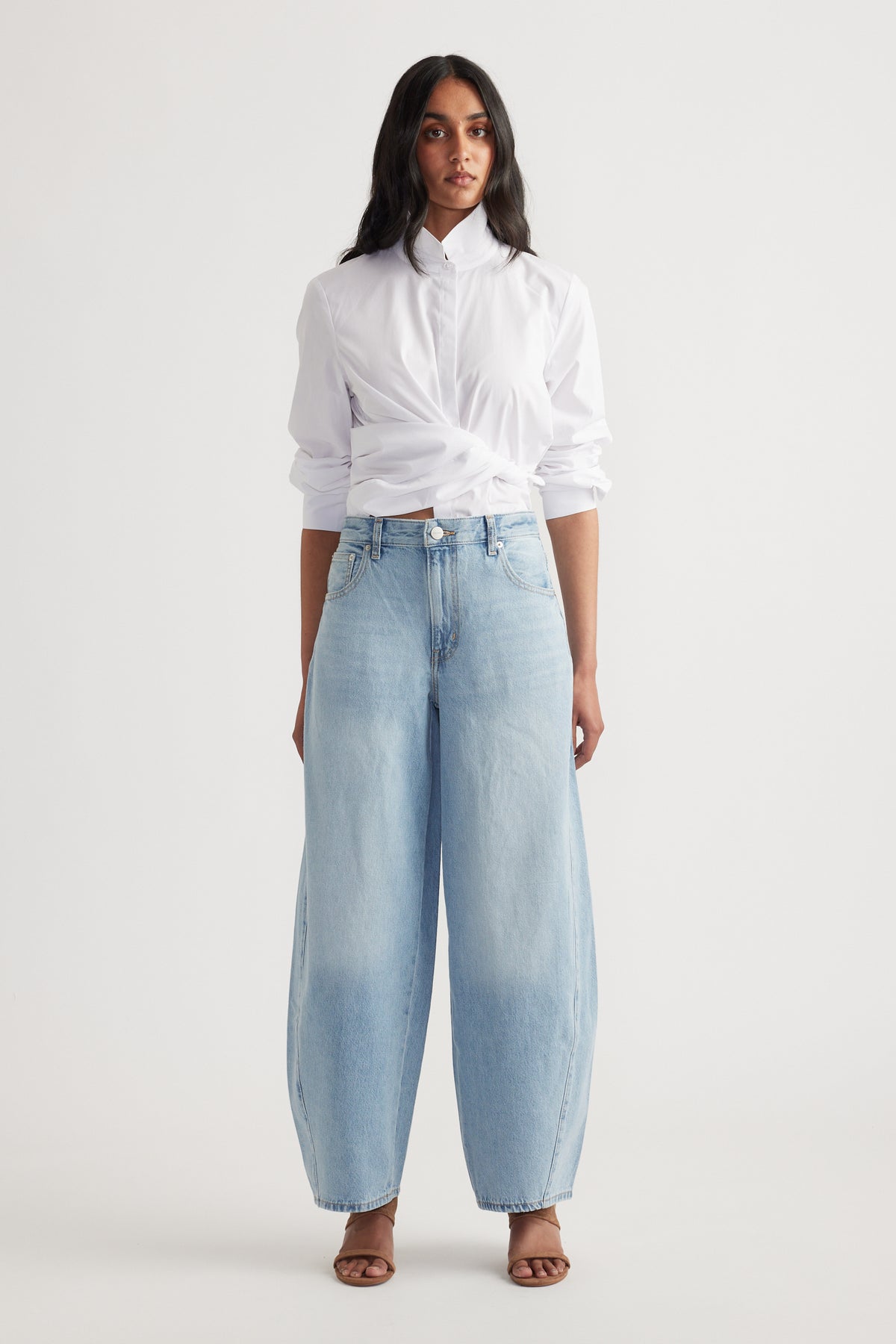 Woman wearing light wash wide-leg denim jeans with a white button-up shirt tucked and rolled sleeves