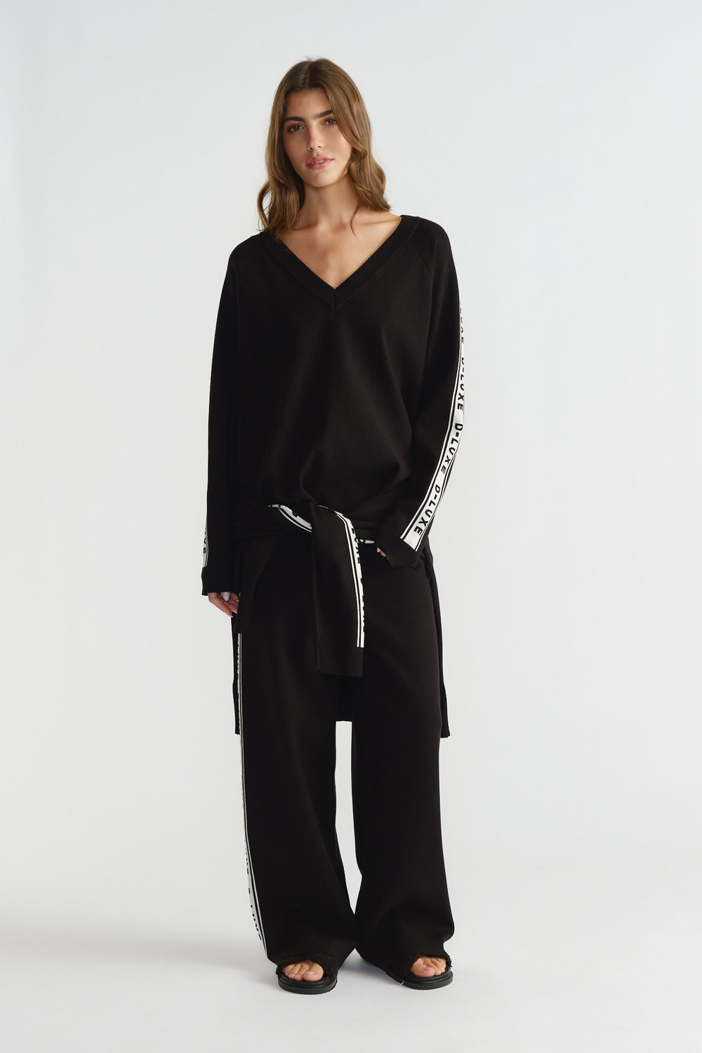 Woman wearing a relaxed black knit top with logo tape details down the sleeves, paired with matching wide-leg pants.